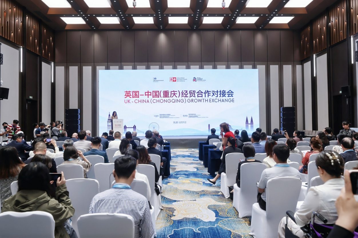 Conference attendees seated in a hall, with speakers and banners in the background.
